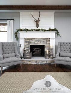 a living room with two chairs, a fireplace and a deer head on the wall