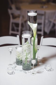 two tall vases filled with flowers and candles on top of a white table cloth