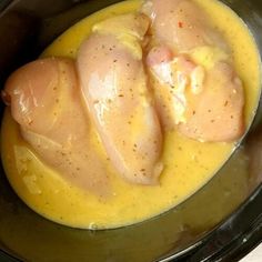 two pieces of chicken sitting in a crock pot filled with yellow liquid and seasoning