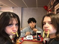 three young people sitting at a table with food and drinks in front of their mouths