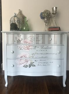 a white dresser with flowers painted on the front and drawers, along with vases