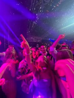 a group of people dancing at a party with purple and blue lights in the background