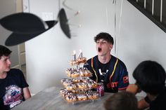 a young man sitting at a table with donuts in front of him and people around him