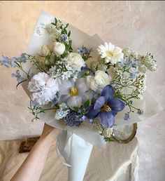 a bouquet of flowers sitting on top of a white vase next to a person's hand