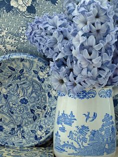 a blue and white vase with purple flowers in it on a table next to plates