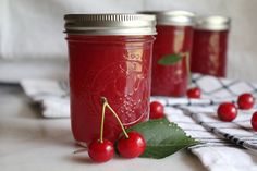 three jars filled with red liquid and cherries on top of a checkered table cloth