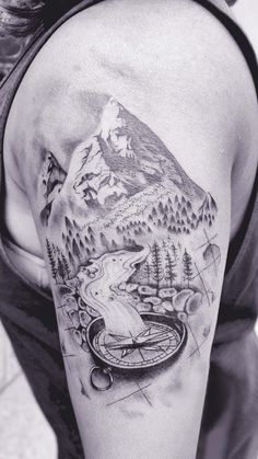 a man with a mountain and compass tattoo on his arm is looking down at the ground