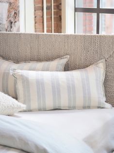 a bed with two pillows on top of it next to a brick wall and window