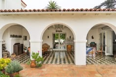 an outdoor patio with potted plants and chairs on the floor, surrounded by arches