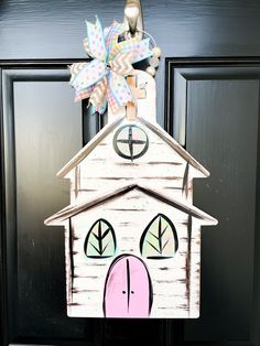 a door hanger with a house painted on it's side and a bow at the top