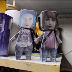 two paper dolls sitting on top of a shelf