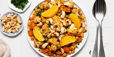 a white plate topped with meat and vegetables next to two bowls filled with cashews