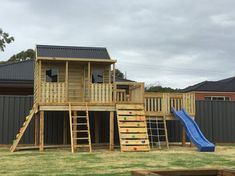 a wooden play set with a slide and climbing wall in the back yard, surrounded by grass