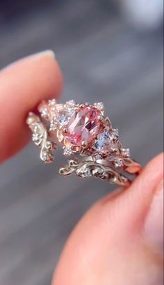 a close up of a person's hand holding a ring with a pink and white diamond