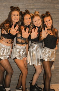 four girls in silver skirts and black tops posing for the camera with their hands up