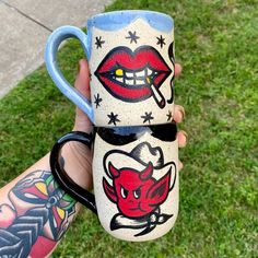 two coffee mugs with designs on them are being held by someone's hand