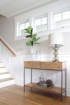 a wooden table with a lamp on top of it next to a stair case and window