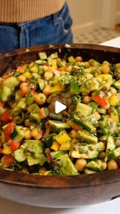 a wooden bowl filled with vegetables on top of a counter next to a woman's stomach