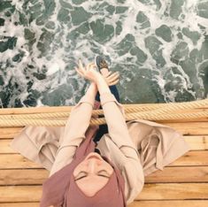 a woman laying on top of a wooden floor next to the ocean with her hands in the air