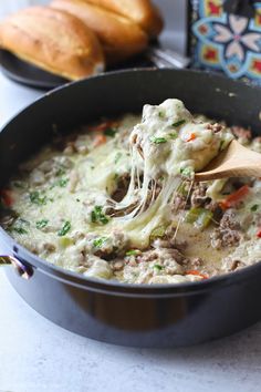 a wooden spoon is being used to scoop some food out of a pot with bread in the background