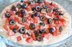 an uncooked pizza with olives, tomatoes and black olives on top