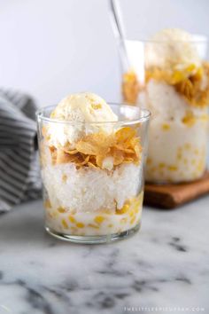 two glasses filled with dessert on top of a marble countertop next to a wooden cutting board