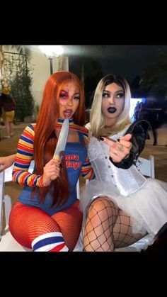 two women dressed in costumes sitting next to each other holding knives and posing for the camera