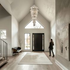 a woman walking through a large open floor plan with chandelier hanging from the ceiling