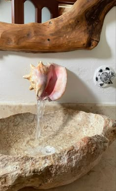 a close up of a stone sink with water coming out of the top and a wooden mirror behind it