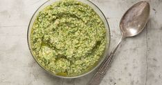 a glass bowl filled with green sauce next to two spoons