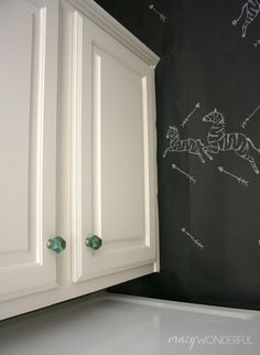 a chalkboard wall in the corner of a kitchen with white cabinets and green knobs