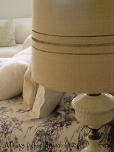 a white lamp sitting on top of a bed next to a night stand and pillows