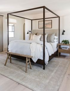 a four poster bed with white linens and pillows in a neutral colored bedroom area