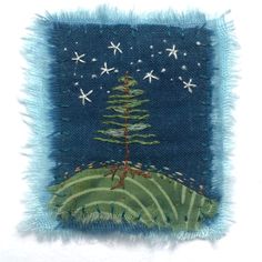 an embroidered christmas tree on a blue and green background with white snowflakes in the sky