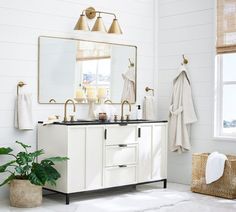 a bathroom with white walls and flooring has gold fixtures on the vanity, along with two candles