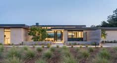 a modern house is lit up at night in the evening with grass and trees surrounding it