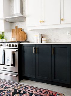 a kitchen with black cabinets and white walls, an area rug in front of the stove