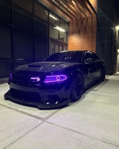 a black car parked in front of a building with purple lights on it's hood