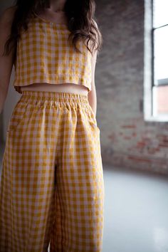 a woman standing in front of a window wearing yellow and white checkered pants with her hands on her hips