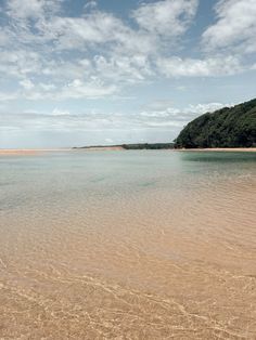 an empty beach with clear water and trees in the background