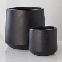 two black vases sitting on top of a white counter