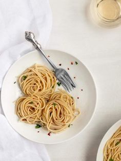 two white plates filled with pasta next to a fork