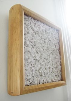 a wooden frame with shredded white paper in it hanging on the side of a wall