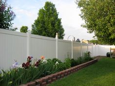 a white picket fence with flowers in the foreground and grass on the other side