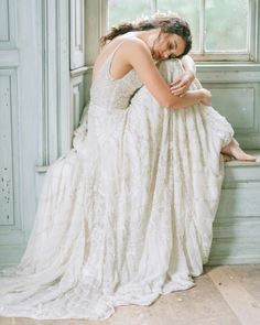 a woman in a wedding dress sitting on a window sill with her arms around her head