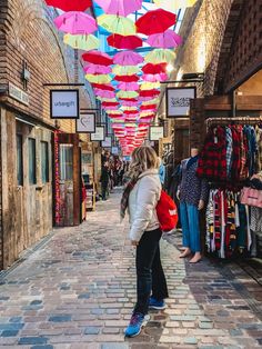 a woman is standing in an alley with many umbrellas hanging from the ceiling above her