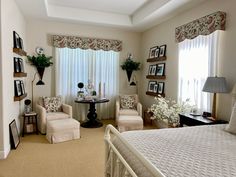 a bed room with a neatly made bed next to two chairs and a table in front of a window