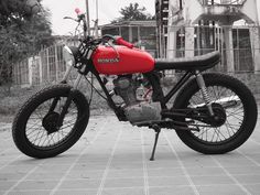 a red and black motorcycle parked on top of a brick road next to a building