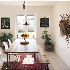 a dining room table with chairs and flowers on the table in front of a window