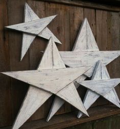 three white wooden stars hanging on the side of a building with wood planks behind them